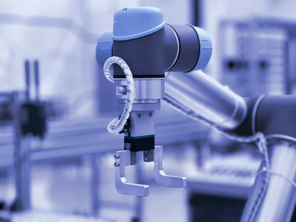 Bras robotisé muni d'une pince dans un atelier, illustrant l'automatisation des processus